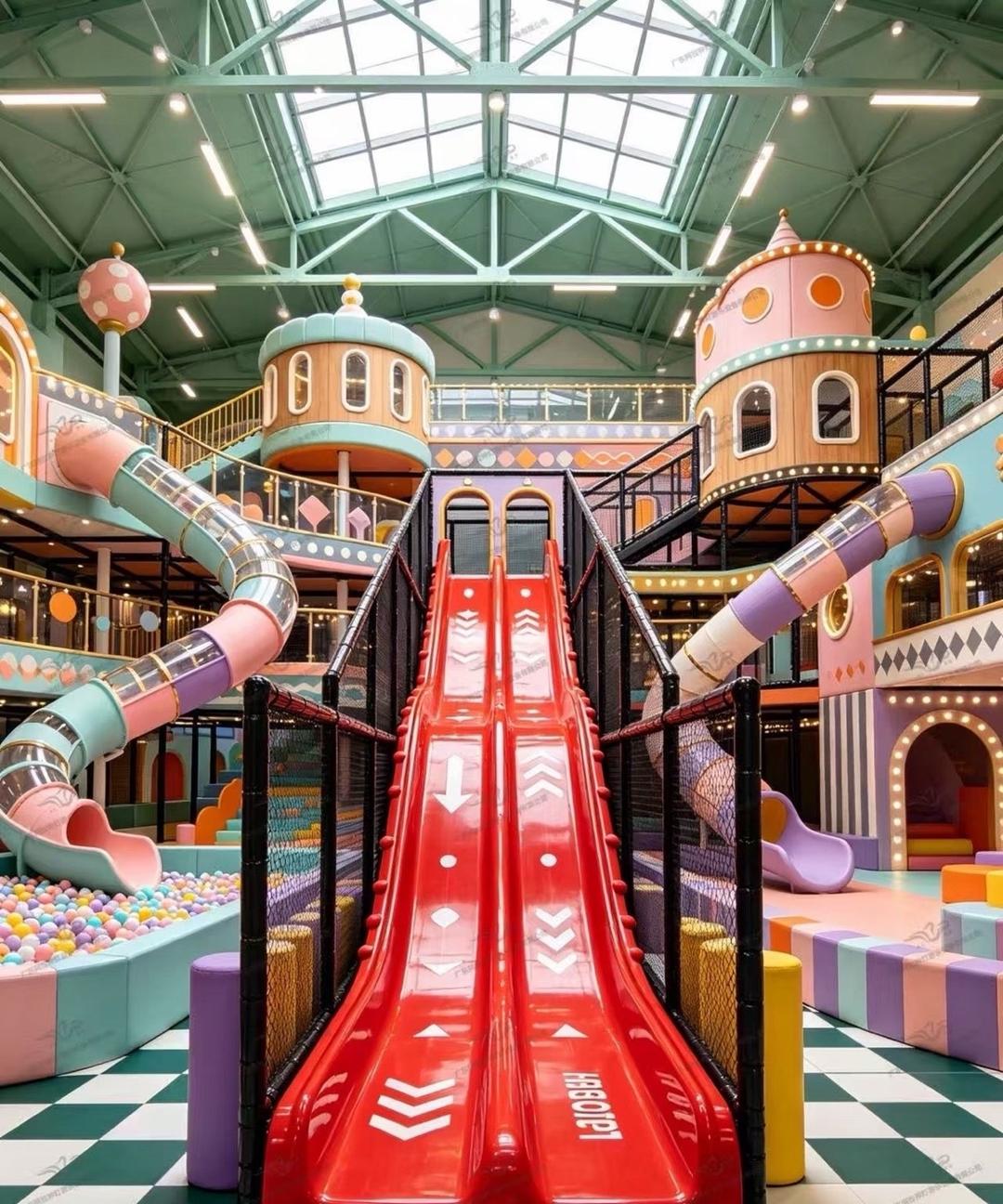 Indoor playground hall with a giant red multi-lane slide and ball pit